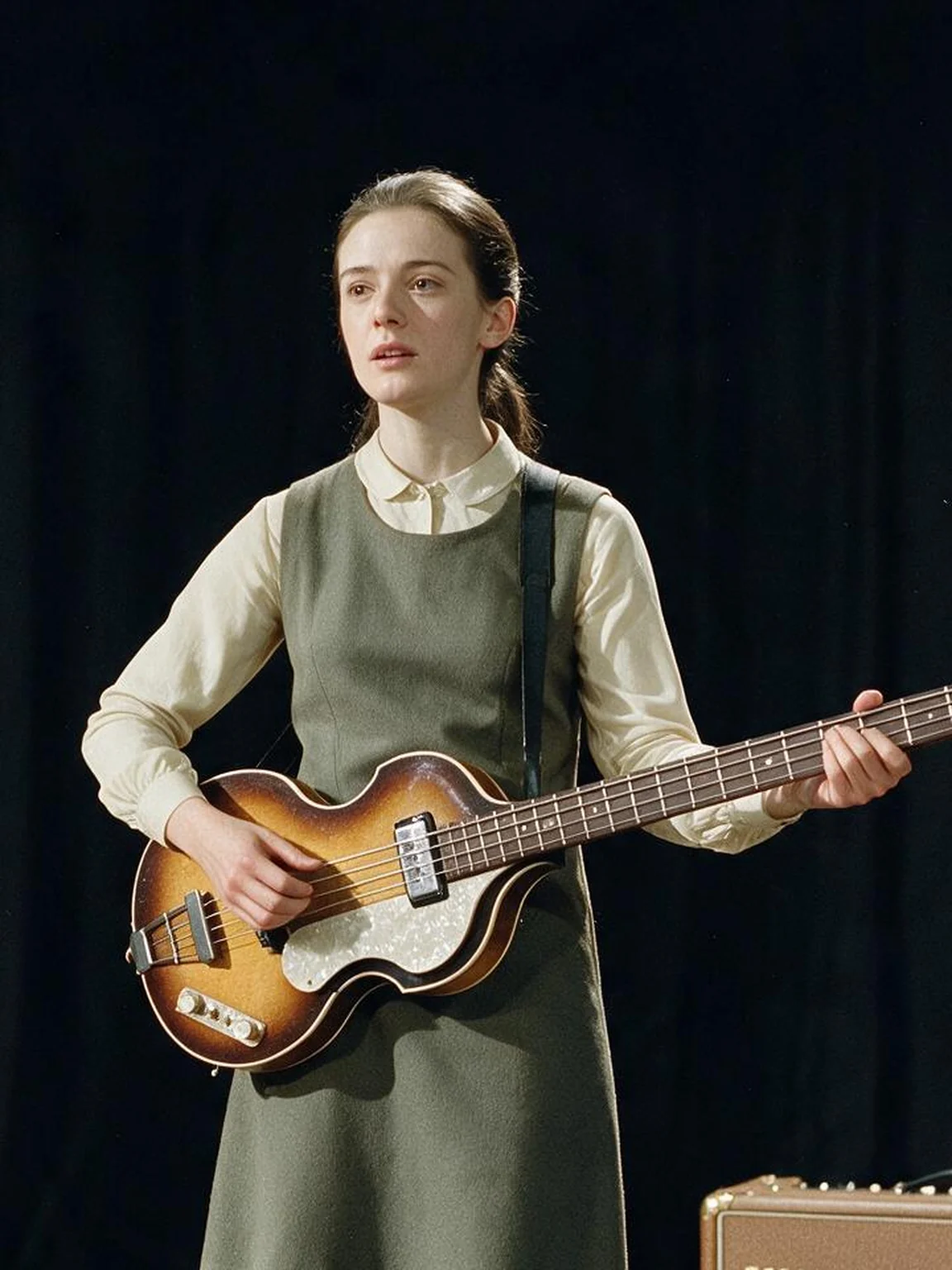 Polly Ticehurst playing a short-scale hollow-body bass beside a Vox amplifier